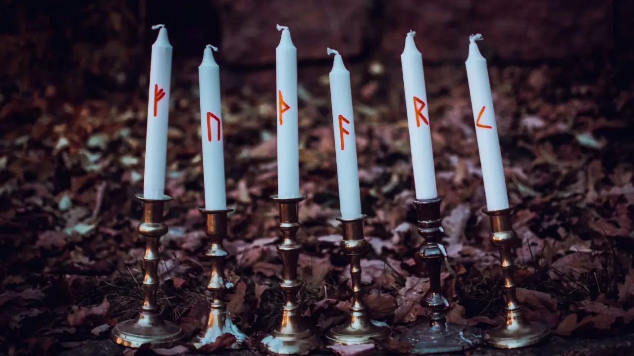 6 white candles in golden candlesticks with the runic text 'FUTHARK' inscribed on them